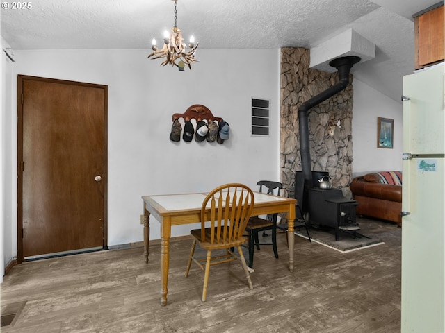 dining area featuring a wood stove, lofted ceiling, a textured ceiling, and wood finished floors