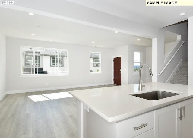 kitchen with white cabinets, sink, an island with sink, and light hardwood / wood-style flooring