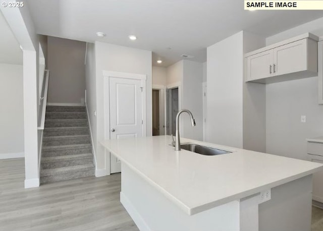 kitchen featuring white cabinetry, light hardwood / wood-style flooring, a kitchen island with sink, and sink