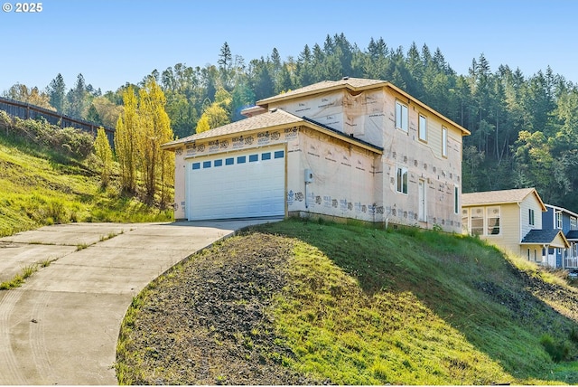 view of front of house featuring a view of trees, an attached garage, and concrete driveway