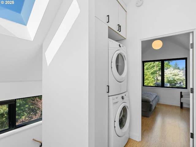 laundry area featuring estacked washer and dryer, light wood-style flooring, baseboards, and cabinet space