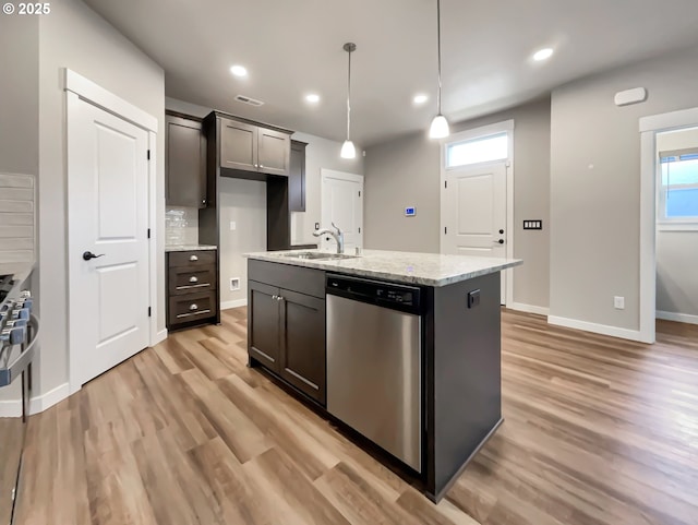 kitchen with pendant lighting, stainless steel dishwasher, a kitchen island with sink, a sink, and light stone countertops