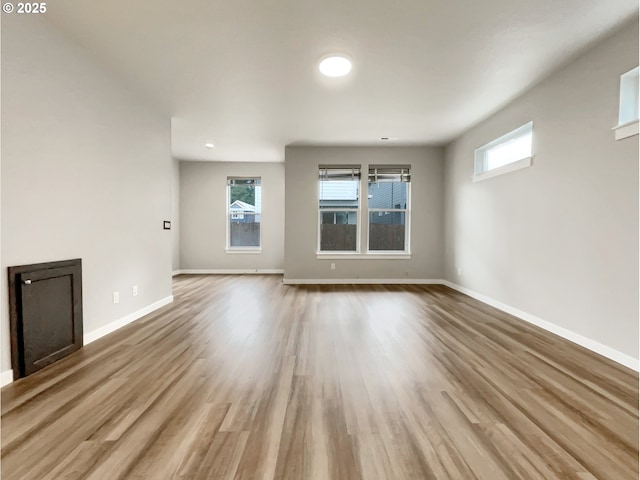 unfurnished living room with a healthy amount of sunlight, light wood finished floors, and baseboards