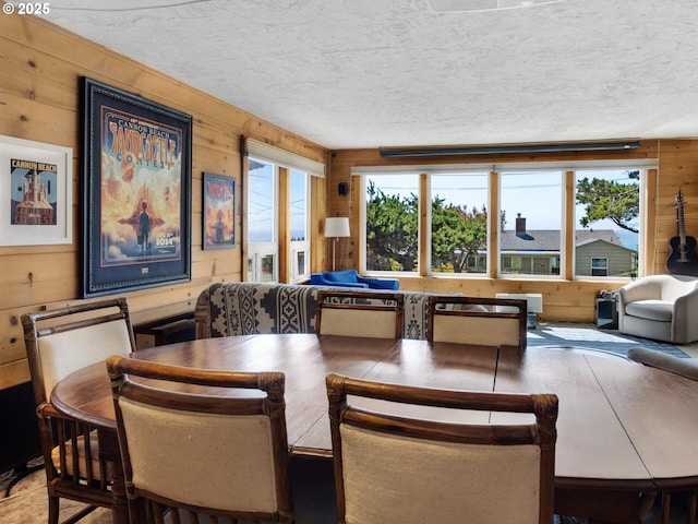 dining space featuring plenty of natural light, wood walls, and a textured ceiling