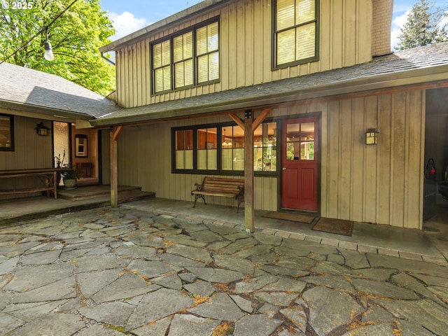 back of house with a patio, board and batten siding, roof with shingles, and a chimney