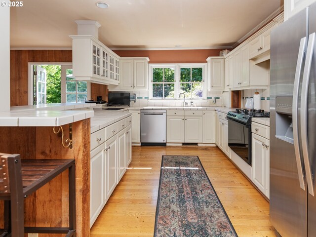 kitchen with light wood-type flooring, white cabinetry, appliances with stainless steel finishes, and a wealth of natural light