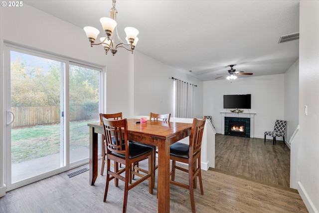 dining room featuring visible vents, light wood-type flooring, a tile fireplace, and ceiling fan with notable chandelier