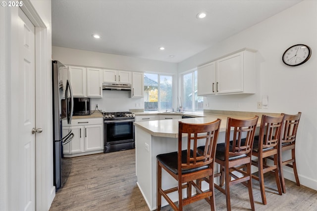 kitchen with a peninsula, light countertops, white cabinetry, under cabinet range hood, and appliances with stainless steel finishes