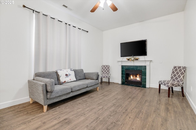living room with a tiled fireplace, ceiling fan, light wood-type flooring, and baseboards