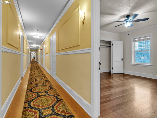 hall featuring a textured ceiling, ornamental molding, light wood-type flooring, and baseboards