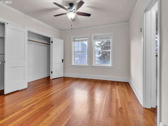 unfurnished bedroom featuring a textured ceiling, ceiling fan, baseboards, ornamental molding, and light wood-type flooring