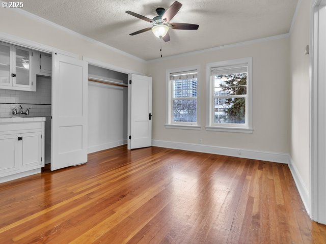 unfurnished bedroom with a textured ceiling, light wood finished floors, ornamental molding, and baseboards