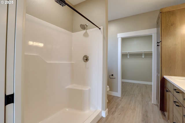 full bath featuring wood finished floors, vanity, baseboards, a spacious closet, and a shower stall