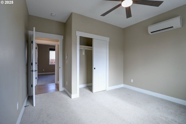 unfurnished bedroom featuring baseboards, light colored carpet, a wall unit AC, ceiling fan, and a closet