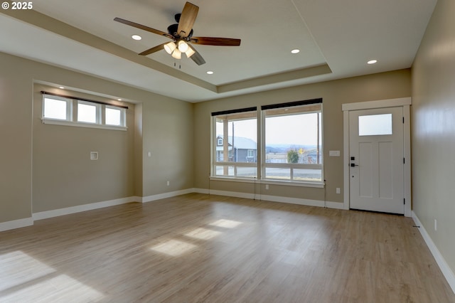 foyer with a healthy amount of sunlight, light wood-type flooring, baseboards, and a raised ceiling