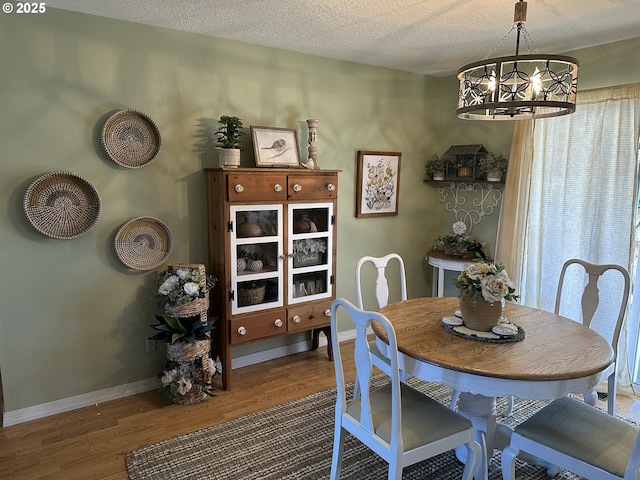 dining space featuring baseboards, a textured ceiling, wood finished floors, and an inviting chandelier