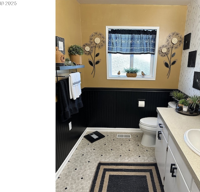 bathroom with wallpapered walls, visible vents, wainscoting, toilet, and vanity