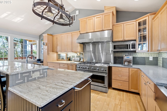 kitchen with vaulted ceiling, stainless steel appliances, light brown cabinetry, and under cabinet range hood