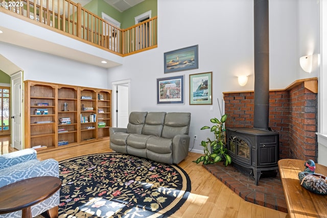 living area featuring a high ceiling, hardwood / wood-style flooring, a wood stove, and baseboards