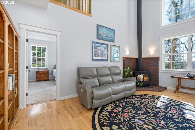 living area with a wood stove, baseboards, light wood-style flooring, and a towering ceiling