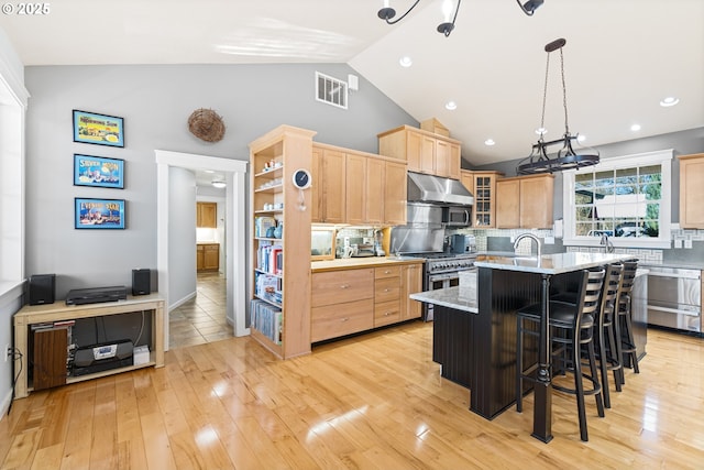 kitchen with visible vents, range with two ovens, light brown cabinetry, under cabinet range hood, and backsplash