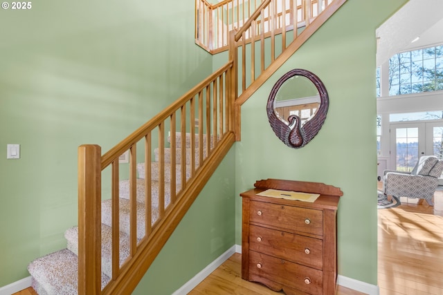 staircase featuring french doors, wood finished floors, a towering ceiling, and baseboards