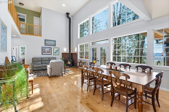 dining room featuring a towering ceiling, a wood stove, french doors, a healthy amount of sunlight, and light wood-style floors