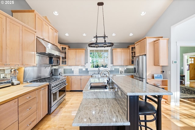 kitchen featuring a breakfast bar area, stainless steel appliances, under cabinet range hood, light brown cabinets, and a sink