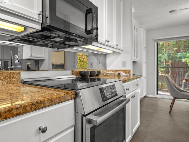 kitchen featuring a textured ceiling, dark tile patterned flooring, stainless steel range with electric stovetop, and white cabinetry