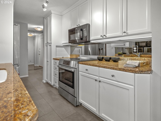 kitchen featuring baseboards, stainless steel appliances, a textured ceiling, white cabinetry, and light tile patterned flooring