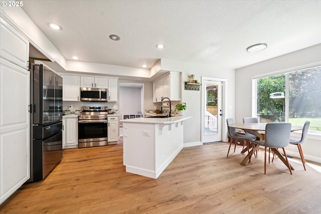 1686 NE 27th Ter, Gresham, OR 97030 - kitchen featuring stainless steel appliances, a peninsula, light countertops, white cabinetry, and light wood-style floors