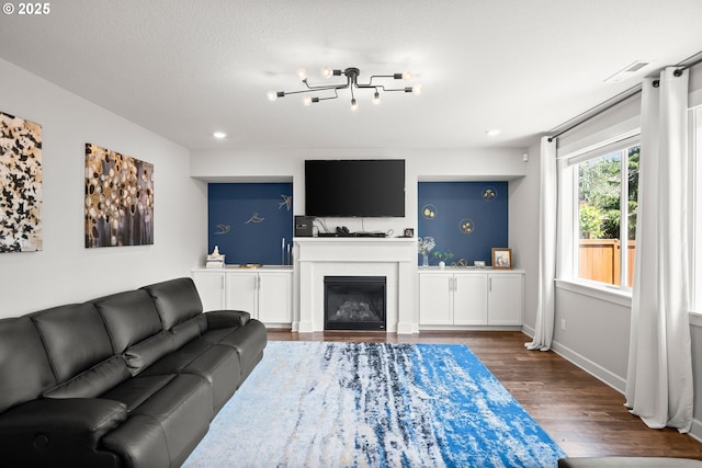 living area with a glass covered fireplace, recessed lighting, baseboards, wood finished floors, and visible vents