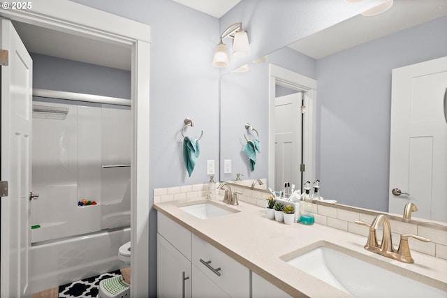 bathroom with a sink, backsplash, toilet, and combined bath / shower with glass door