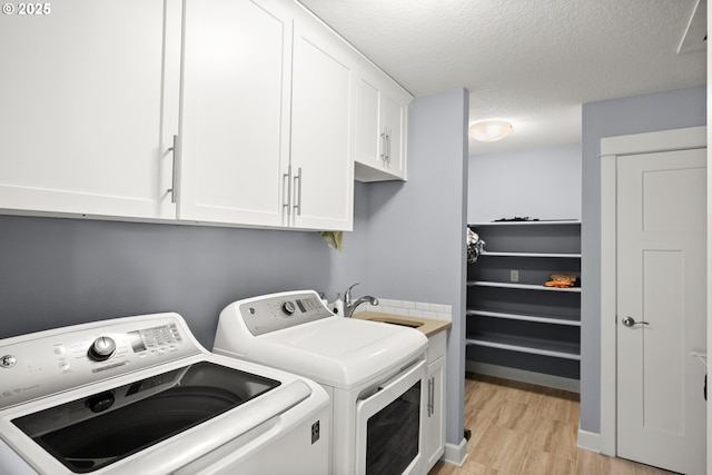 laundry area featuring a textured ceiling, cabinet space, a sink, light wood-style floors, and washer and clothes dryer