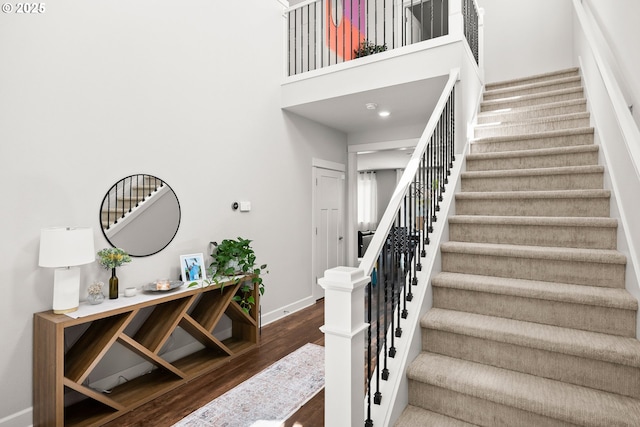 staircase with baseboards, wood finished floors, and a high ceiling