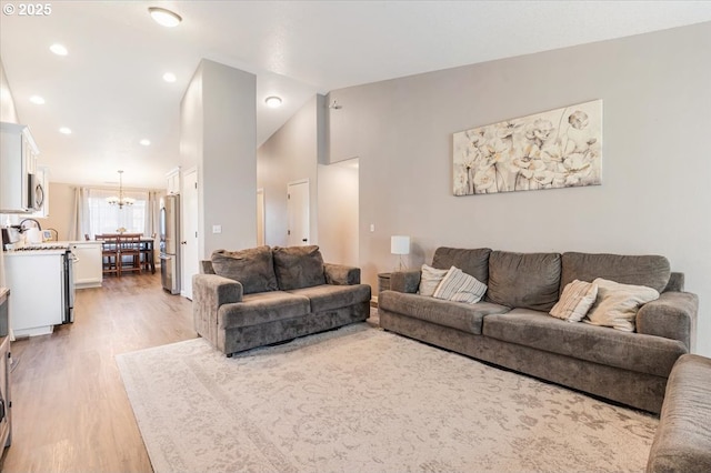 living room featuring lofted ceiling, light hardwood / wood-style floors, and a chandelier