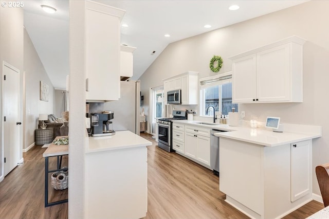 kitchen featuring lofted ceiling, white cabinetry, light wood-type flooring, kitchen peninsula, and stainless steel appliances