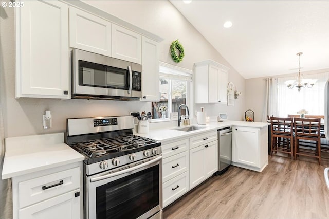 kitchen featuring lofted ceiling, sink, appliances with stainless steel finishes, white cabinetry, and kitchen peninsula