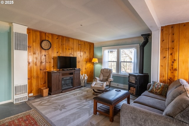 living room featuring a wood stove, wooden walls, a heating unit, and a glass covered fireplace