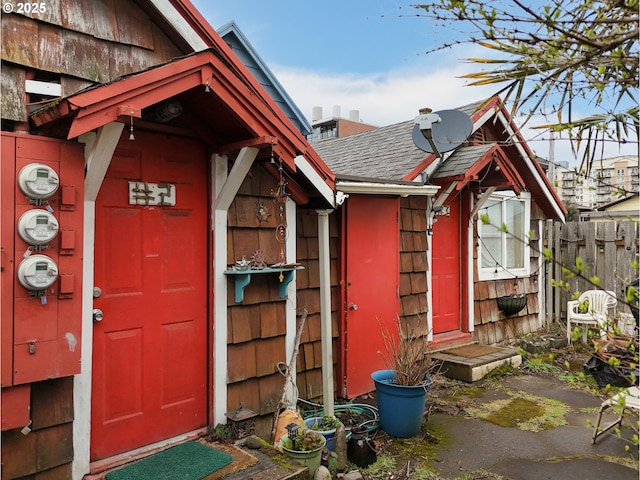 view of exterior entry with roof with shingles and fence