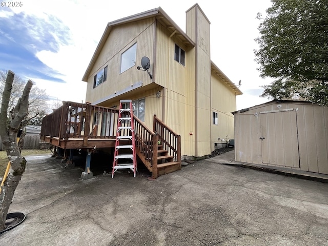 back of property with an outdoor structure, a chimney, a wooden deck, and a shed