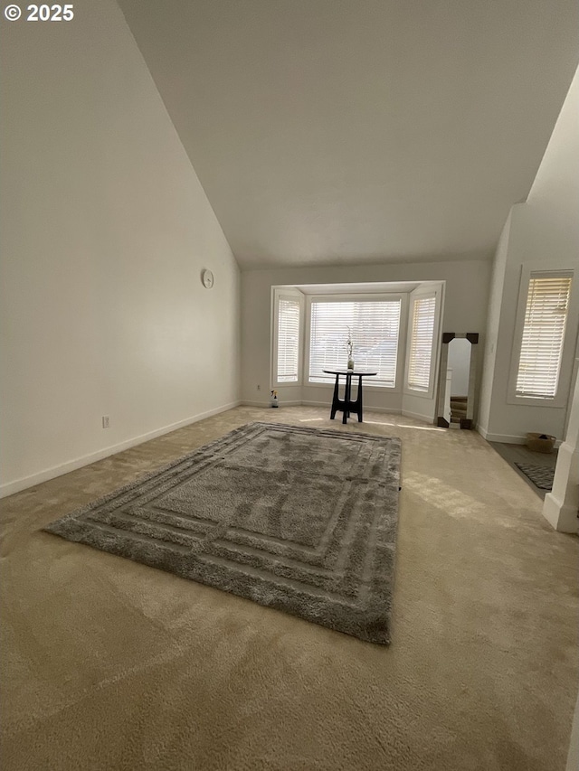 unfurnished living room featuring carpet, high vaulted ceiling, and baseboards