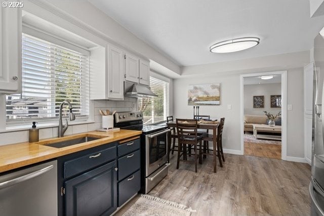 561 E Ridgeway Ave, Hermiston, OR 97838 - kitchen featuring appliances with stainless steel finishes, under cabinet range hood, white cabinets, light wood finished floors, and tasteful backsplash