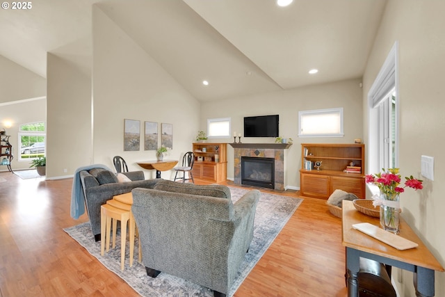 living room featuring light wood finished floors, a tiled fireplace, recessed lighting, baseboards, and high vaulted ceiling
