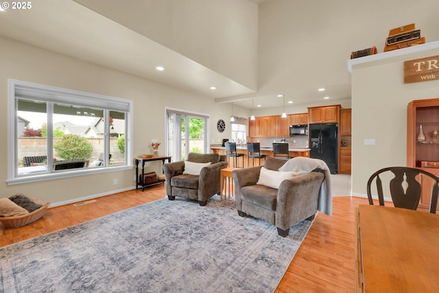 living area with light wood finished floors, baseboards, recessed lighting, and a towering ceiling