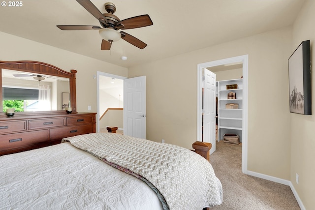 bedroom featuring light colored carpet, a walk in closet, baseboards, and a ceiling fan