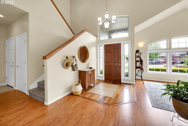entrance foyer featuring a high ceiling, light wood-style floors, a chandelier, stairway, and baseboards