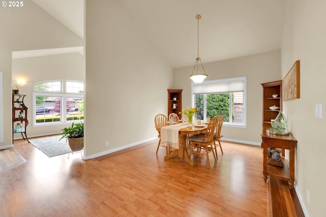 dining room featuring high vaulted ceiling, light wood-style floors, and baseboards