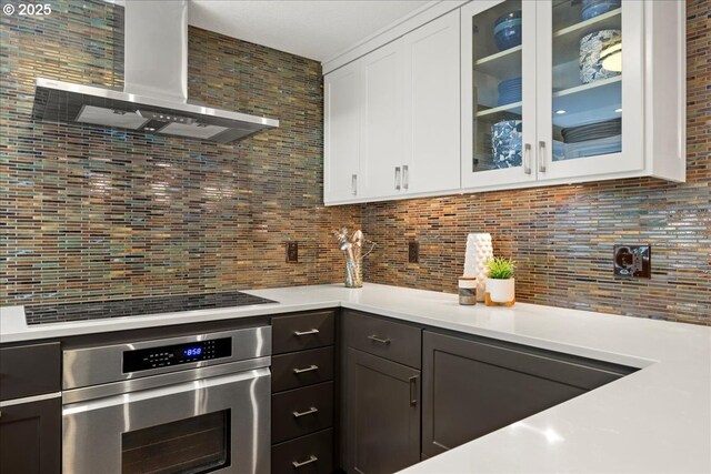 bar with decorative backsplash, stovetop, oven, and wall chimney exhaust hood