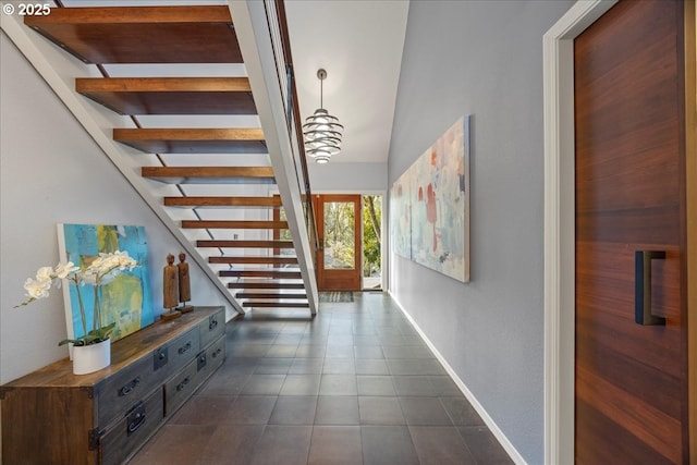 hall with stairs, baseboards, and dark tile patterned flooring
